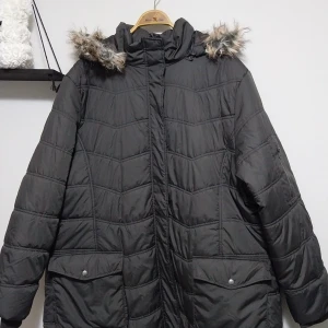 Svart quiltad dunjacka med fuskpäls - Säljer en svart quiltad dunjacka med fuskpäls på huvan. Jackan har långa ärmar och praktiska fickor med dragkedja. Perfekt för kalla dagar. Strl XL.