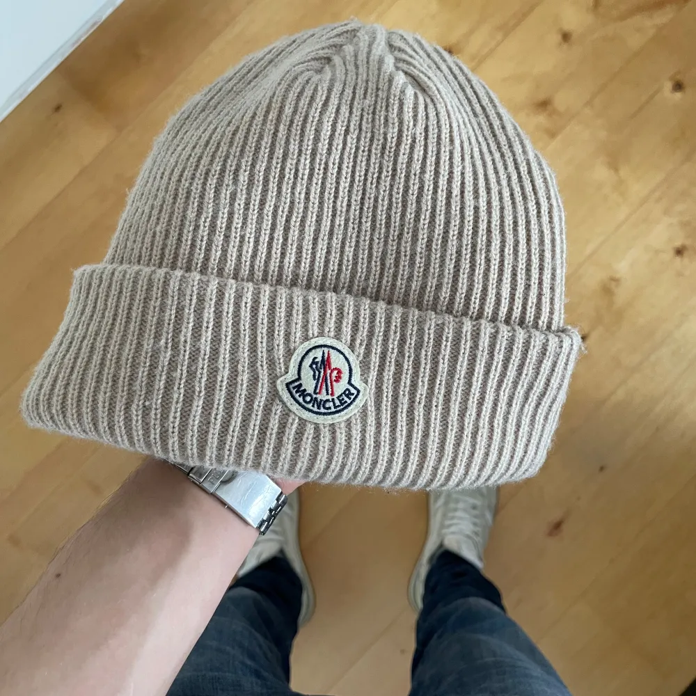 Snygg beige ribbad mössa från Moncler med broderad logotyp framtill. Perfekt för att hålla värmen under kyliga dagar. Stilren design som passar till det mesta. Skick 10/10. Asusteet.