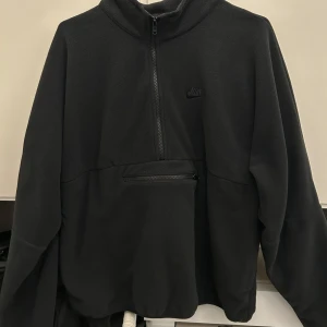 Svart fleece hoodie från Nike - Säljer en svart fleece hoodie från Nike med halv dragkedja och en praktisk ficka framtill. Perfekt för kyliga dagar och har en stilren design med diskret logga på bröstet.
