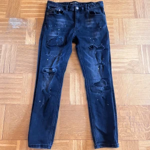 Svarta jeans från Supply & Demand - Coola svarta jeans från Supply & Demand med slitna detaljer och färgstänk för en edgy look. De har en slim passform och är perfekta för en trendig stil. Midjan är normal och de har klassiska fem fickor.