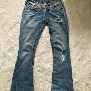 Blå jeans med slitningar från True Religion - Snygga blå jeans från True Religion med slitningar på framsidan och bakfickor med dekorativa sömmar. bootcut/flare säljer för de var för stora❤️ w27