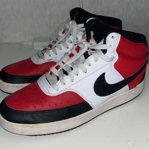 Nike sneakers i rött, vitt och svart (Jordan) 1 - Snygga Nike sneakers i en klassisk färgkombination av rött, vitt och svart. Skorna har en hög modell med snörning och den ikoniska Nike-loggan på sidan. Perfekta för en sportig look.