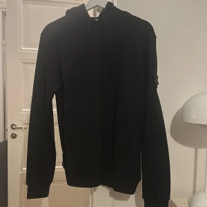 Stone Island hoodie - Säljer en stilren svart hoodie från Stone Island med deras ikoniska märke på ärmen. 