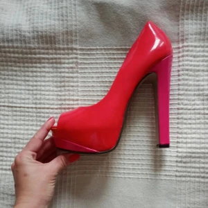 Högklackade lackpumps från Ideal - Snygga  pumps i orange och shockrosa med hög klack och öppen tå från Ideal. Skorna har en glansig finish och en djärv rosa klack som ger en extra touch. Perfekta för att göra ett statement.