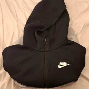 Svart och grå hoodie från Nike - Säljer en snygg svart och grå hoodie från Nike med dragkedja. Den har en klassisk design med Nike-logga på bröstet och en bekväm huva. Perfekt för en avslappnad stil. Vi kan diskutera priset.