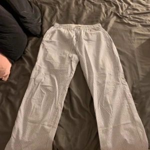  Pyjamasbyxor i blått och vitt - Säljer ett par bekväma randiga byxor i blått och vitt. Byxorna har en elastisk midja för extra komfort och är perfekta för en avslappnad stil. De är tillverkade i ett lätt material som passar bra för varmare väder.