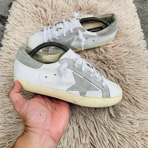 Vita sneakers med stjärndetalj - Snygga vita sneakers med grå stjärndetalj på sidan och matchande grå häl. Skorna har vita snören och en krämfärgad sula. Perfekta för en avslappnad stil.