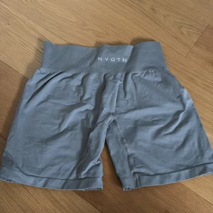 Grå shorts från NVGTN - Säljer ett par grå shorts från NVGTN. De har en bred resår i midjan med logotypen framtill. Perfekta för träning eller en avslappnad dag. Materialet är mjukt och stretchigt för bästa komfort.