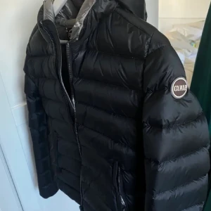 Svart dunjacka från Colmar - Snygg svart dunjacka från Colmar med dragkedja och huva. Jackan har en quiltad design och en rund logotyp på ärmen. Perfekt för kyligare dagar. Jackan har ett litet hål i innerfickan. Men inget som varken syns när den är på eller stör andvändningen. Passar xs/s