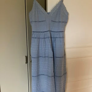 Ljusblå klänning med smala axelband - Vackert mönstrad ljusblå klänning med fint fall, smala axelband och v-ringning. Klänningen är perfekt för varma dagar. Den har en luftig passform och en dragkedja i ryggen för enkel påklädning.