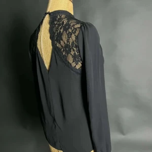 Svart blus - Elegant svart blus med spetsdetaljer på axlarna och långärmad design. Perfekt för en stilren look med en touch av romantik.