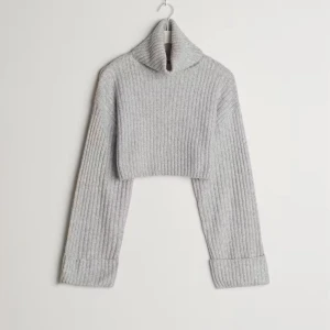 Grå ribbad croppad polotröja - Säljer en stilren grå ribbad polotröja med croppad design. Tröjan har långa ärmar och en hög krage. Är aldrig använd och därför i perfekt skick! Köparen står för frakt 