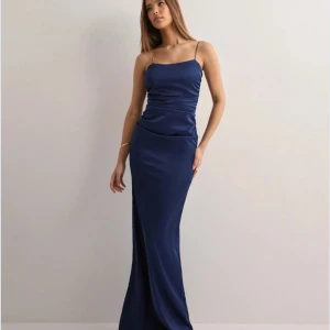 långklänning med smala axelband - Säljer denna  långklänning i svart med smala axelband och figurnära passform. Klänningen har en stilren design i ett glansigt material som ger en lyxig känsla. Perfekt för bal. Endast använd en gång 