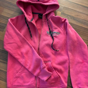 Rosa hoodie från Peak Performance - Säljer en snygg rosa hoodie från Peak Performance med dragkedja och broderad logga på bröstet. Den har en justerbar huva med snören och praktiska fickor framtill. Perfekt för en avslappnad stil!              dragkedjan är sönder