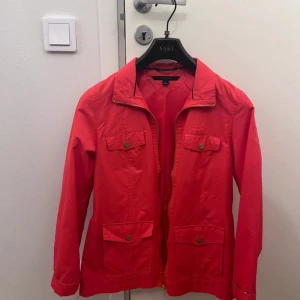 Röd jacka från Tommy Hilfiger - Snygg röd jacka från Tommy Hilfiger med dragkedja och knappar. Jackan har långa ärmar och praktiska fickor framtill. Perfekt för en stilren look.