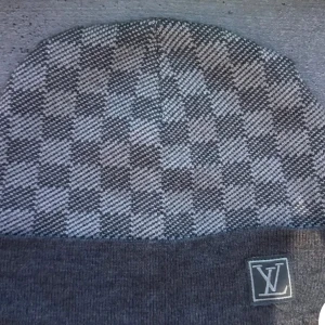 Grå rutig mössa  - Snygg grå mössa  med ett klassiskt rutigt mönster. Mössan har en uppvikt kant. Perfekt för att hålla stilen i kallare väder.