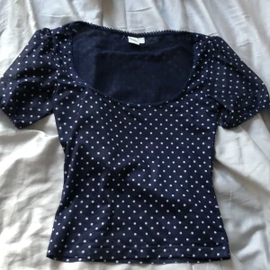 Mörkblå prickig topp från Twik - Säljer en söt mörkblå topp med vita prickar från Twik. Toppen har korta ärmar och en rundad halsringning med dekorativ kant. Perfekt för en avslappnad stil.