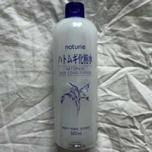 Naturie Hatomugi Skin Conditioner - En stor flaska på 500 ml av Naturie Hatomugi Skin Conditioner. Denna produkt är känd för att återfukta och mjukgöra huden. Perfekt för daglig användning och kan appliceras på både ansikte och kropp. Flaskan har en enkel design med blå text och en bild av en växt. Endast använd ett fåtal gånger (se bild 3)