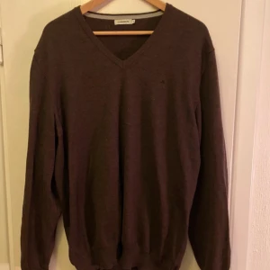 Brun tröja från J.Lindeberg - Säljer en stilren brun tröja från J.Lindeberg. Tröjan har en v-ringad design och långa ärmar, perfekt för kyligare dagar. Den är tillverkad i ett mjukt material som ger en bekväm passform. Passar utmärkt för både vardag och mer uppklädda tillfällen.