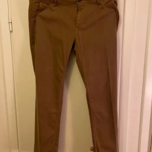 Bruna chinos från Hugo Boss - Snygga bruna chinos från Hugo Boss med en klassisk design. Byxorna har en rak passform och är tillverkade i ett bekvämt bomullsmaterial. Perfekta för en stilren look.