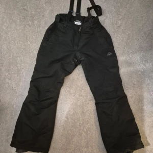 Svarta täckbyxor från McKinley - Säljer ett par svarta täckbyxor från McKinley med justerbara hängslen och dragkedja. Perfekta för vinterns kalla dagar. Byxorna har en praktisk design med fickor och förstärkta knän. Några vita fläckar vid grenen men har ej testat ta bort det. 