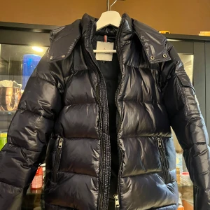 Mörkblå  dunjacka från Moncler - Säljer en snygg mörkblå  dunjacka från Moncler med glansig finish. Jackan har en dragkedja framtill och två praktiska fickor med dragkedjor. Perfekt för kalla dagar! Den är helt ny och har även NFC 