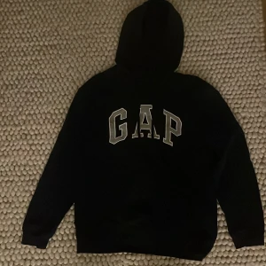 GAP Hoodie - Säljer en klassisk marinblå hoodie från GAP då den tyvärr inte kommer till användning.. Hoodien har en bekväm passform och är tillverkad i mjukt material. Själv har jag aldrig använt den men då den är köpt här på Plick så finns det tyvärr ett hål på sidan av hoodien (se bild) annars är den i fint skick. Priset kan diskuteras.