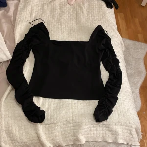 Svart långärmad topp med rynkade ärmar - Snygg svart topp med långa rynkade ärmar och en elegant design. Perfekt för en stilren look.