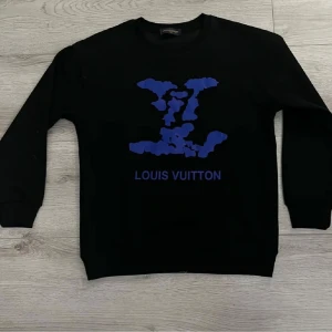 Svart tröja från Louis Vuitton med blått tryck - Snygg svart tröja från Louis Vuitton med ett unikt blått tryck på framsidan. Tröjan har långa ärmar och en klassisk rund halsringning. Perfekt för en stilren look.