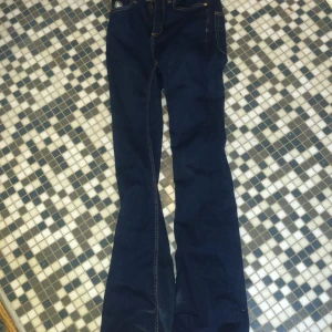 Mörkblå bootcut jeans - Snygga mörkblå bootcut jeans med klassisk femficksdesign och kontrasterande sömmar. Perfekta för en avslappnad stil med en touch av retro. De har en dragkedja och knapp framtill.
