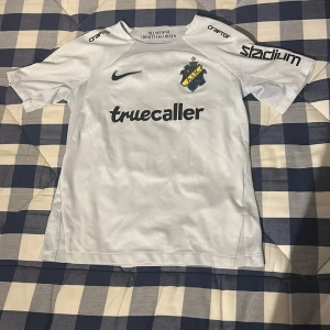 Vit AIK fotbollströja med tryck - Säljer en vit AIK fotbollströja från Nike med korta ärmar. Tröjan har tryck av 'truecaller' och 'Stadium' på framsidan samt 'Milošević' och nummer 5 på baksidan. 