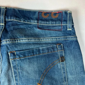 Blå jeans med slitningar från dondup  - Snygga blå jeans från Dondup med coola slitningar och en klassisk femficksdesign. De har en knappgylf och är perfekta för en avslappnad stil. Detaljer som kontrastsömmar och en liten logga på baksidan ger extra karaktär. Pris kan alltid diskuteras✅