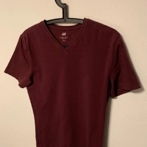 Vinröd t-shirt från H&M - Säljer en stilren vinröd t-shirt från H&M i storlek S. T-shirten har en v-ringad hals och korta ärmar, perfekt för en avslappnad look. Tillverkad i ett mjukt material som känns skönt mot huden.