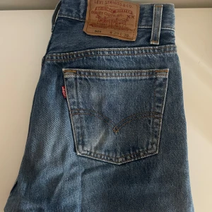 Levis 501 jeans - Klassiska Levis 501 jeans i blå denim. Dessa jeans har en rak passform och är lågmidjade med knappgylf. Perfekta för en tidlös stil.