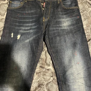 Blå jeans från Dsquared2 - Snygga blå jeans från Dsquared2 med coola slitningar och unika detaljer. Baktill finns ett stort gult och rött märke med texten 'DSQUARED2'. De var använda bara 1 gång. De e helt nya