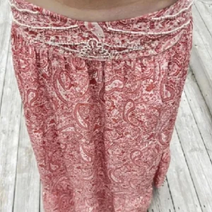 Röd paisleymönstrad långkjol - Snygg röd långkjol med paisleymönster. Kjolen har en bred midja och ett flödande fall som ger en bohemisk känsla. Perfekt för en avslappnad stil. Saknar lite pärlor med inget man tänker på❤️