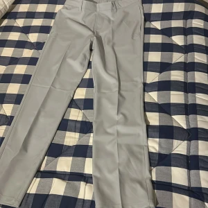 Grå byxor från Adidas Golf  - Snygga grå byxor från Adidas Golf med en stilren design. Byxorna har en normal passform och är tillverkade i ett syntetmaterial som ger en bekväm känsla. Perfekta på golfbanan, byxorna är helt nya.