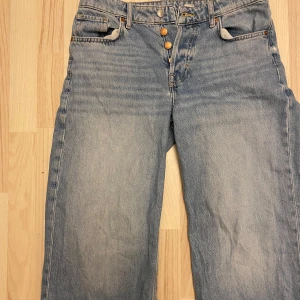 Blå jeans med knappar - Säljer ett par klassiska blå jeans med knappgylf. De har en baggy passform och är lågmidjade. Perfekta för en casual look. De är i bra skick. 