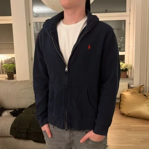 Mörkblå hoodie från Polo Ralph Lauren - Säljer en snygg mörkblå hoodie från Polo Ralph Lauren med dragkedja och broderad röd logga på bröstet. Perfekt för en avslappnad stil. Hoodien har långa ärmar och en bekväm passform. Xl junior eller S 