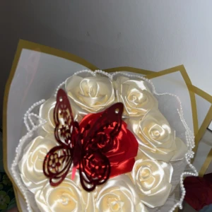 Dekorativ bukett med rosor och fjäril. - En vacker dekorativ bukett med vita och en röd ros, prydd med en elegant röd fjäril. Perfekt som en romantisk present eller som dekoration i hemmet.