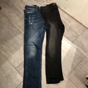 Två par jeans i blått och svart - Säljer två par jeans, ett i klassiskt blått med slitningar och ett i svart.