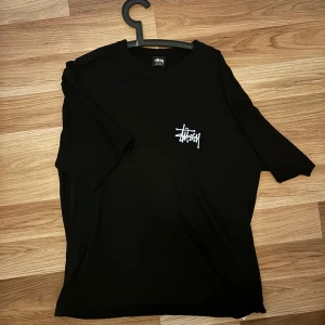 Svart t-shirt från Stussy - Snygg svart t-shirt från Stussy med deras ikoniska logga i vitt på bröstet och ryggen. Perfekt för en avslappnad stil. T-shirten har korta ärmar och en normal passform. Stl Xl 