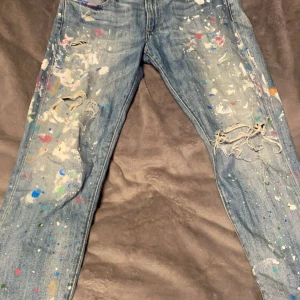 Jeans med färgstänk från Polo Ralph Lauren - Unika jeans från Polo Ralph Lauren med coola färgstänk och slitna detaljer. Perfekt för en avslappnad och kreativ stil. Klassisk blå denim med en twist av färg och textur.