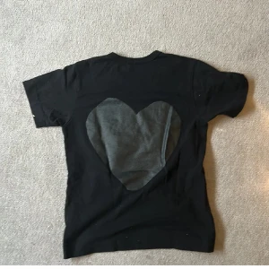 svart tshirt från cdg  - Snygg svart t-shirt från comme de garcons med ett stort hjärtmönster på framsidan. T-shirten har korta ärmar och en klassisk passform. för mer frågor är de bara och skriva