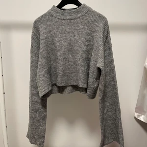 Stickad tröja från H&M - Säljer en grå croppad stickad tröja från H&M i storlek S. Tröjan har långa ärmar som är vidare mot slutet och en liten krage. Bara att skriva om fler bilder önskas💕