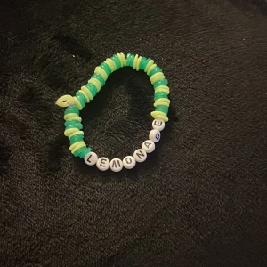 En armband som säger lemonade  - Säljer ett färgglatt armband med bokstavspärlor som bildar ordet 'LEMONADE'. Armbandet har gröna och gula pärlor som ger en somrig känsla. Perfekt accessoar för att liva upp din outfit!