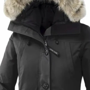 Svart parkajacka från Canada Goose - Säljer en svart parkajacka från Canada Goose med pälskantad huva. Jackan har dragkedja och knappar framtill samt två fickor med lock. Perfekt för kalla vinterdagar. Märkeslogga på ärmen ger en extra touch av stil.