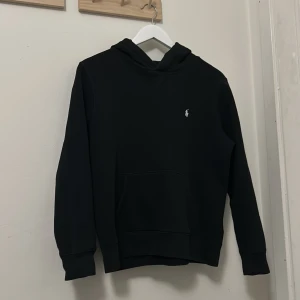 Svart hoodie från Ralph Lauren - Säljer en stilren svart hoodie från Ralph Lauren med det klassiska logotypbroderiet på bröstet. Tröjan har en bekväm passform med långa ärmar och en praktisk magficka. Perfekt för en avslappnad look. Nypriset ligger på ca 1200