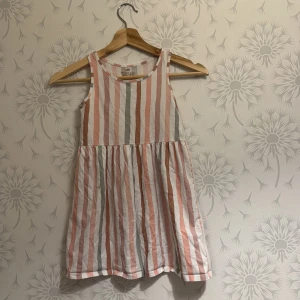 Rosa, beige och grå klänning - Söta klänning med fina ränder i rosa, beige och grå toner.  Klänningen har ett löst, bekvämt snitt med en fin volang i nederkant. Perfekt för varma sommardagar eller festliga tillfällen.