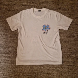 Vit t-shirt med blomtryck från Stüssy - Stussy t-shirt med blå rosa blommor print. Storlek S och är i bra skick. Skicka gärna om ni har frågor!